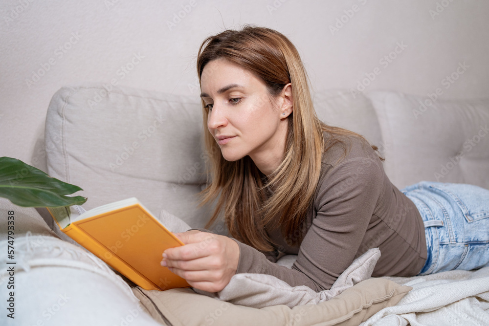  Woman relaxing on sofa and reading novel book at home.