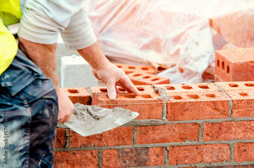 Close up of industrial bricklayer laying bricks on cement mix on construction site photo