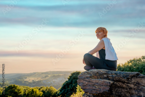 happy haired woman in sports suit sitting on a cliff after exercises