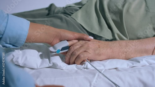 Closeup to the camera old hand patient wearing the finger heart rate and young hand holding and supporting the patient in the hospital room video details capturing