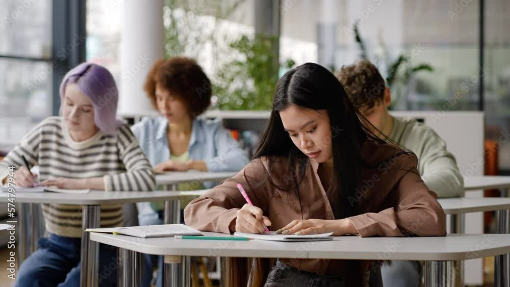 Young diverse students taking notes during lecture in the library campus of high school institution Young diverse students taking notes during lecture in the library campus of high school institution