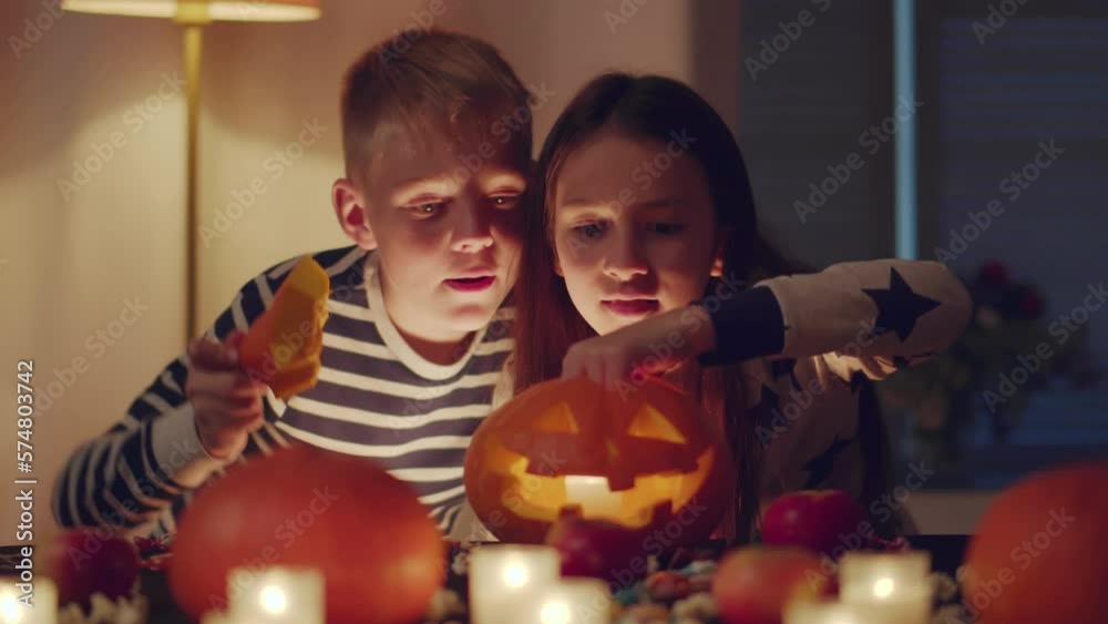 Preteen brother and sister put candle in halloween pumpkin. Realtime