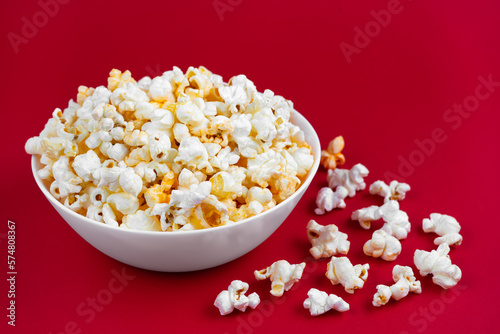 Scattered tasty cheese popcorn in white bowl isolated on red background. Flat lay, top view. Fast food, movie, cinema concept