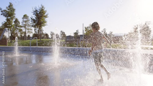 Following 9 year old boy runing thorough multiple splash pad water jets