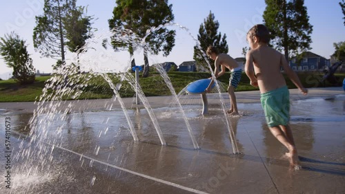 6 year old child runs under water arches at splash pad in slow motion