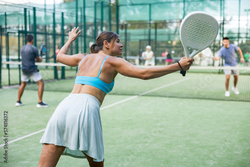 Sportive slim woman with racquet playing padel in court. View from the back