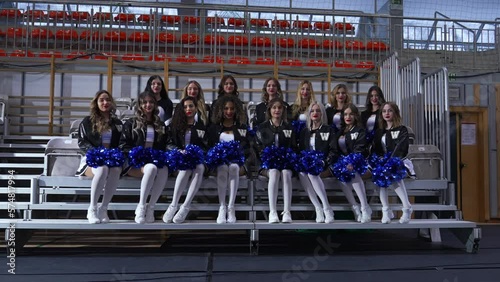 Wallpaper Mural cheerleaders in black and white uniforms holding blue pompoms and sitting confidently for photos. High quality 4k footage Torontodigital.ca