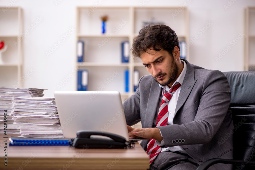 Young male employee unhappy with excessive work in the office Young male employee unhappy with excessive work in the office