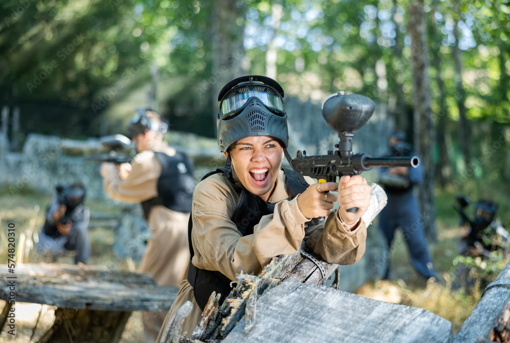 Fototapeta premium Young woman fires a gun with passion while playing paintball