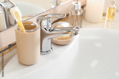 Holder with toothbrushes on white ceramic sink, closeup