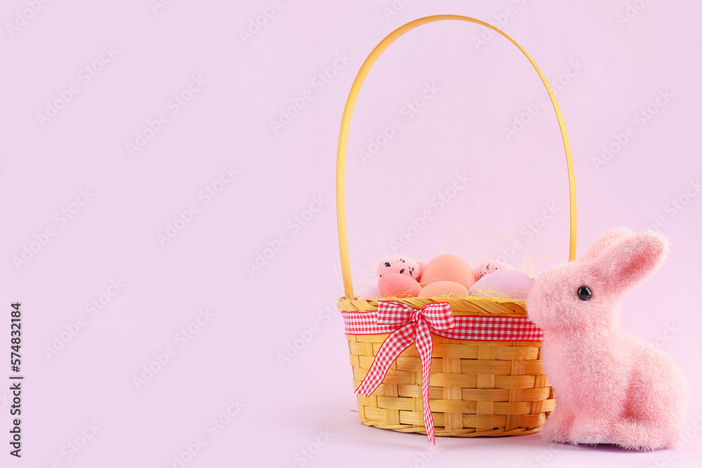 Basket with Easter eggs and toy bunny on pink background Basket with Easter eggs and toy bunny on pink background