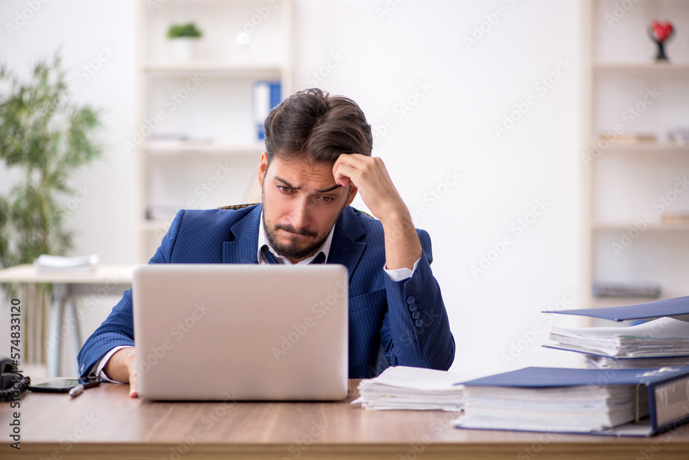 Young male employee unhappy with excessive work in the office Young male employee unhappy with excessive work in the office
