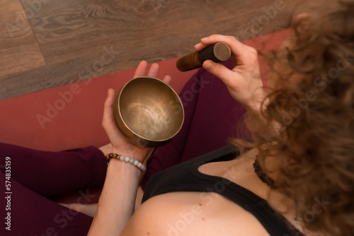 Curly woman sitting on floor and using singing bowl for relaxation and meditation.