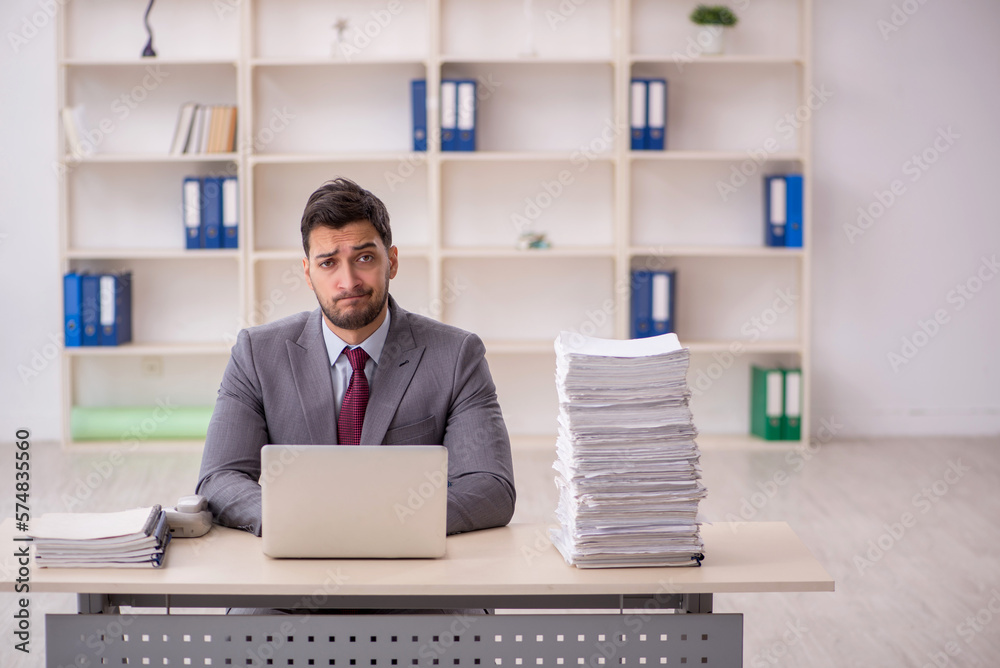 Young male employee unhappy with excessive work in the office Young male employee unhappy with excessive work in the office