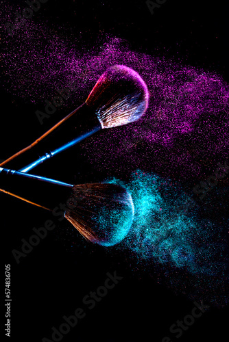 Makeup brush cosmetics and explosion of colorful powder on dark background