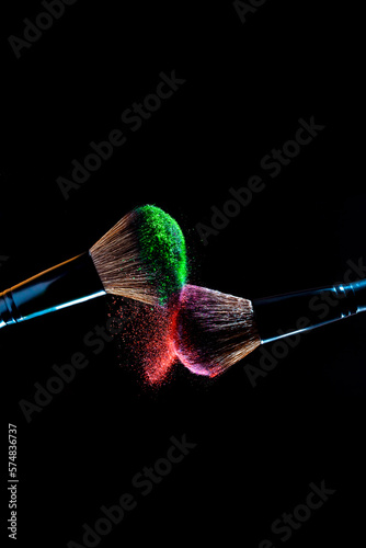 Cosmetics makeup brushes with green and red colored powder on a dark background