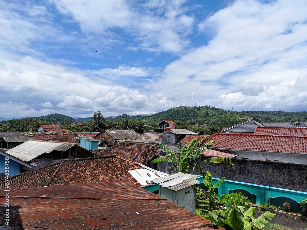 Obraz premium A charming residential district with colorful roofs and buildings against a backdrop of fluffy clouds, creating an idyllic scene.