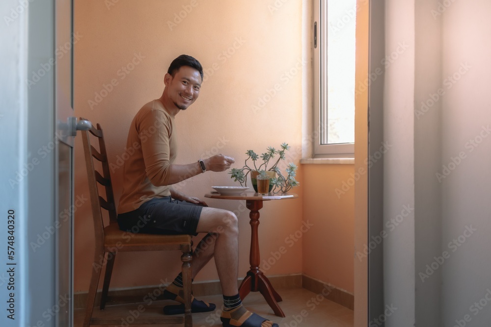 Asian man having breakfast soup on the terrace by the windows. Asian man having breakfast soup on the terrace by the windows.