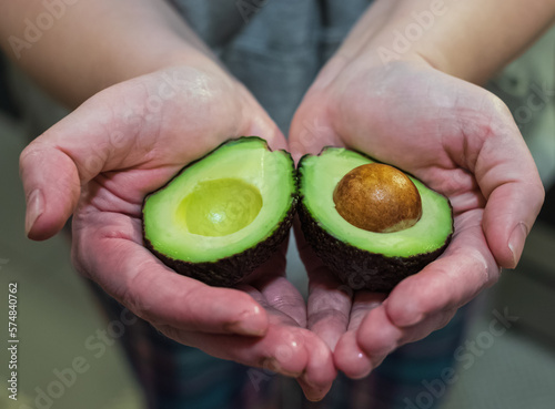 Avocado in heart shape in hands of a woman. Top view of fresh sliced avocado. Vegetarian food. Two halves of avocado