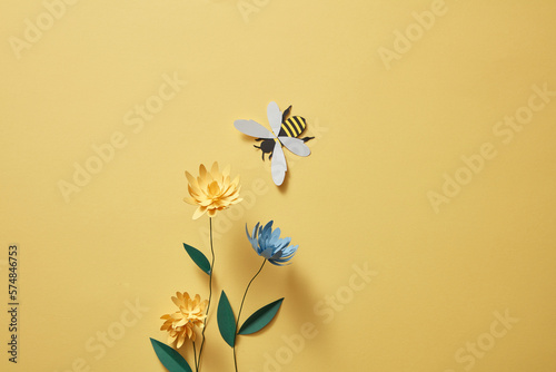 Fototapeta Naklejka Na Ścianę i Meble -  Flowers with many colors and a paper bee on light yellow background. Empty area for product or text. Graphic design for spring
