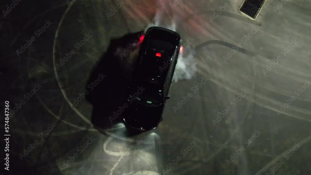 Aerial view above a car drifting at a parking lot, during nighttime - top down, drone shot