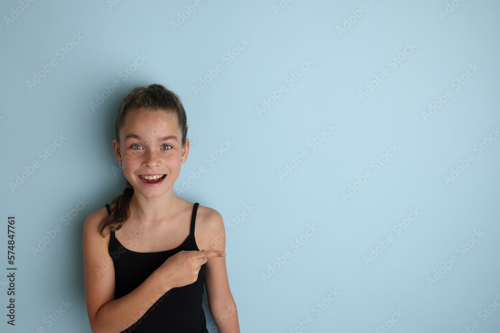 Little emotional teenage girl in a black t-shirt 11, 12 years old on an isolated blue background. Children's studio portrait. Place the text to copy the place for the inscription Little emotional teenage girl in a black t-shirt 11, 12 years old on an isolated blue background. Children's studio portrait. Place the text to copy the place for the inscription