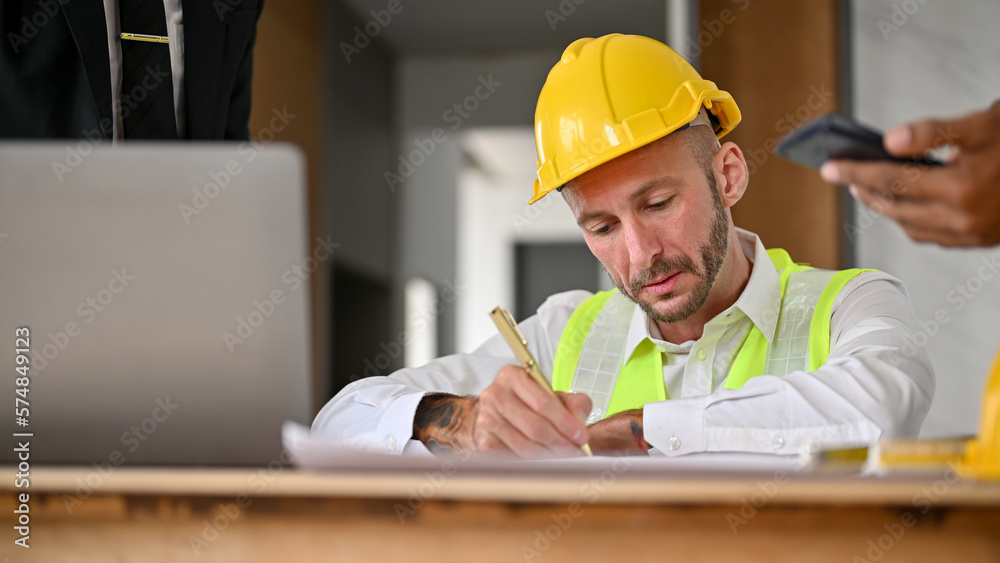 Professional Caucasian male construction engineer is drawing the building's scale on a blueprint. Professional Caucasian male construction engineer is drawing the building's scale on a blueprint.