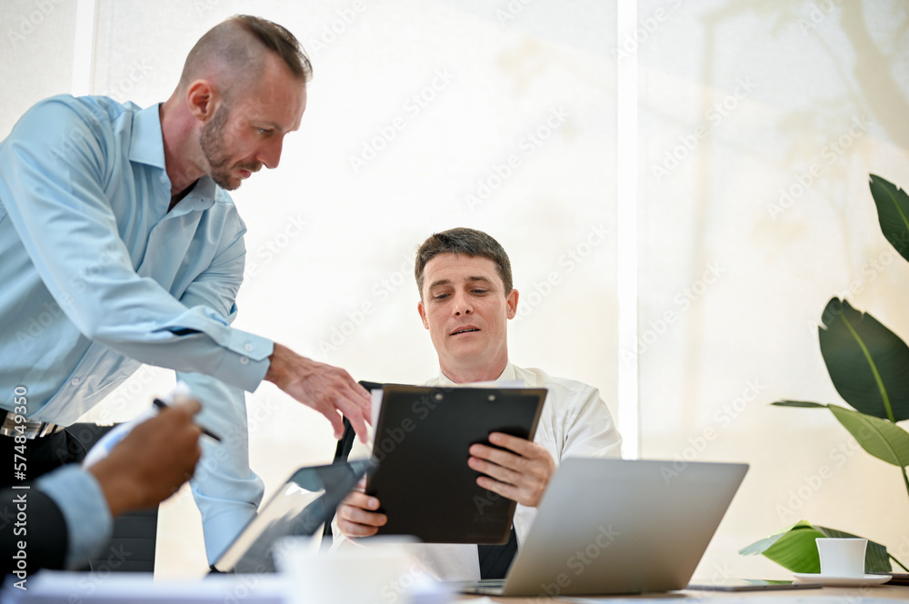 Smart Caucasian businessman is talking with his colleague, looking the details on document Smart Caucasian businessman is talking with his colleague, looking the details on document