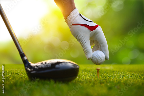 Close-up hand putting golf ball on tee with drivers.