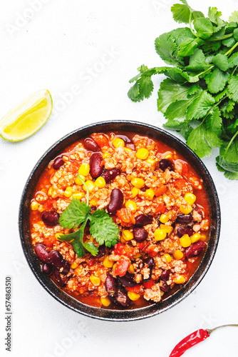 Chili con carne with beef, red beans, paprika, corn and hot peppers in tomato sauce, spicy tex-mex dish, white table background, top view