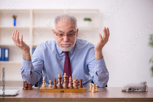 Old businessman employee playing chess at workplace