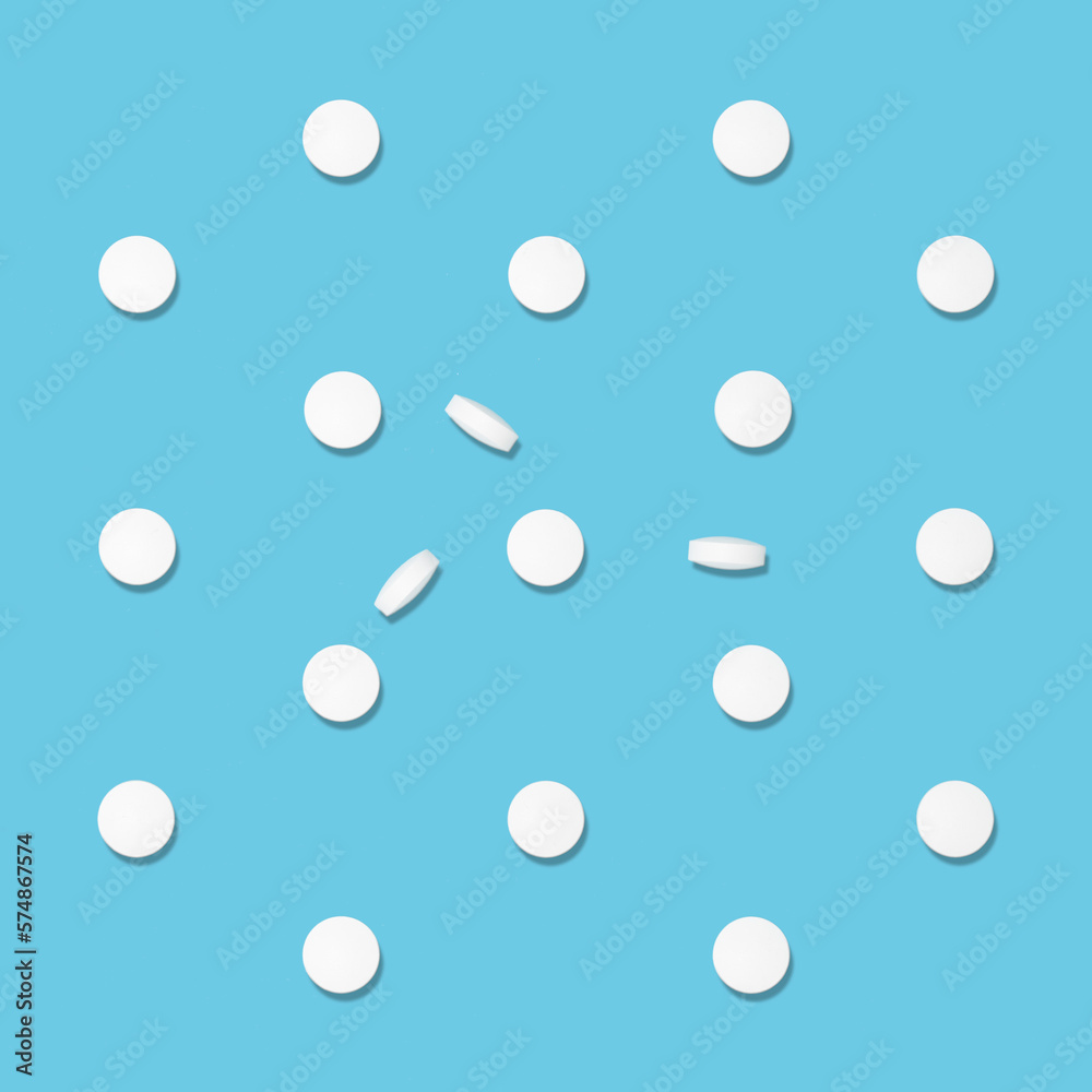White tablets pattern in hard light on soft light blue color, top view. Medical and pharmacy remedies, home medicine chest.