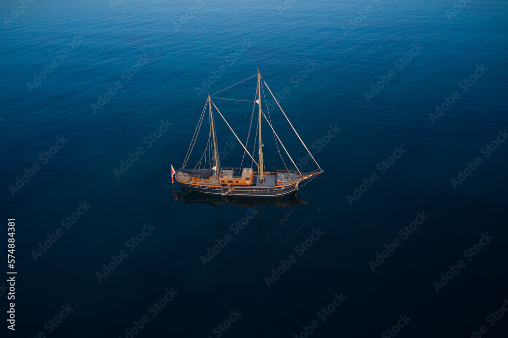 Large wooden sailing yacht anchored top view. Sailing yacht on dark water aerial view. Large wooden sailing yacht anchored top view. Sailing yacht on dark water aerial view.