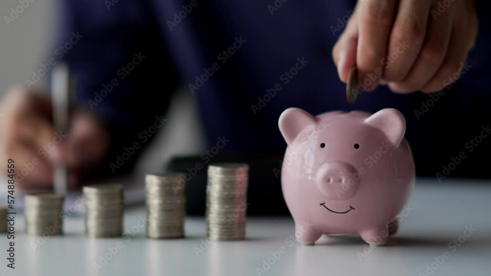 Businessman hands puts a coin in a pink piggy bank. The concept of saving money or savings.