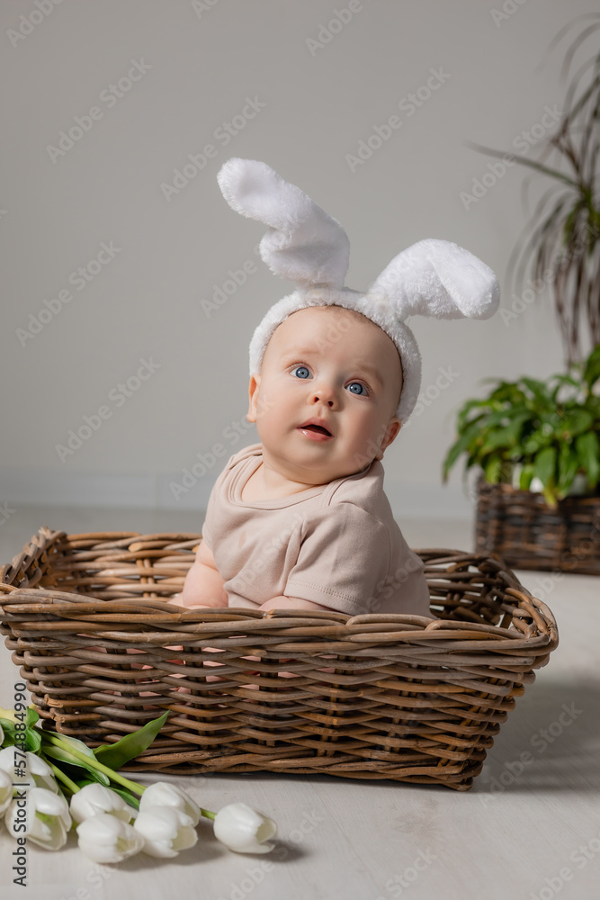 baby in bodysuit with rabbit ears is sitting in wicker basket on the floor with a bouquet of tulips baby in bodysuit with rabbit ears is sitting in wicker basket on the floor with a bouquet of tulips