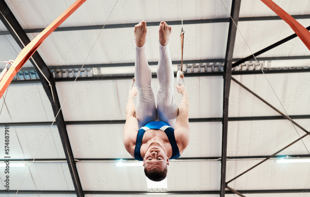 Man, acrobat and gymnastics upside down on rings in fitness for practice,  training or workout at gym. Professional male gymnast hanging on ring  circles for athletics, acrobatics or strength exercise Stock Photo