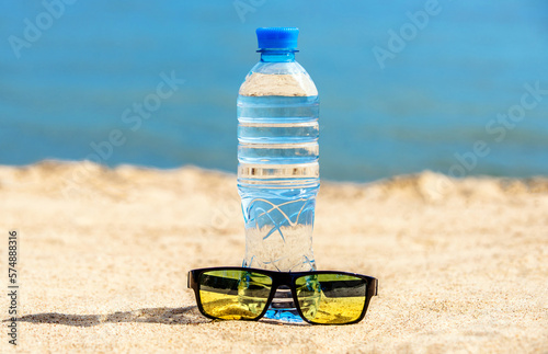 A bottle of drinking water and sunglasses on the sea beach