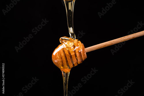 Foto Wooden dipper with honey falling down isolated on black background