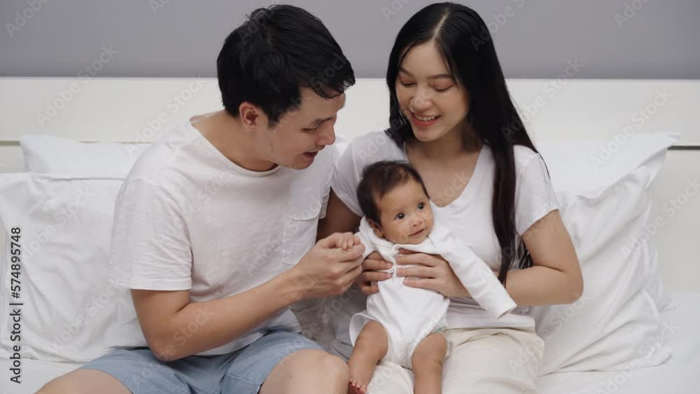 happy parents (father and mother) talking and playing with baby on a bed happy parents (father and mother) talking and playing with baby on a bed