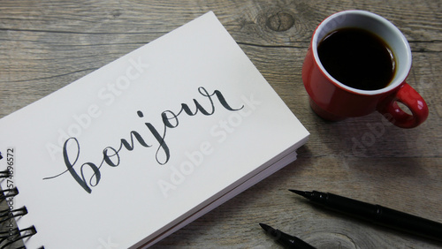 BONJOUR lettrage sur cahier avec tasse de café et stylos photo