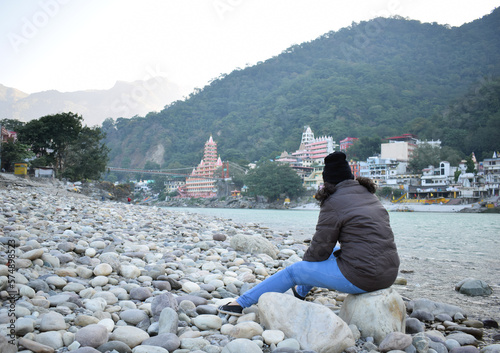Photography Girl Sitting on the River beach looking at the Mountains of Himalayas, In Rishik