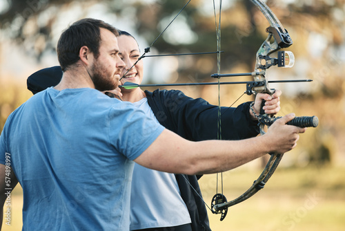 Archery, bow and shooting range sports training with a woman and man outdoor for target practice. Archer and athlete person with focus on field for competition or game to aim arrow for action photo