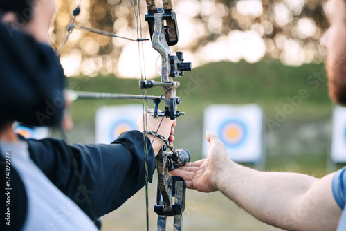 Archer hands, coach and bow or arrow learning for archery competition, athlete focus challenge or girl training practice. Teacher, teaching and man coaching woman on sports, aim and target shooting