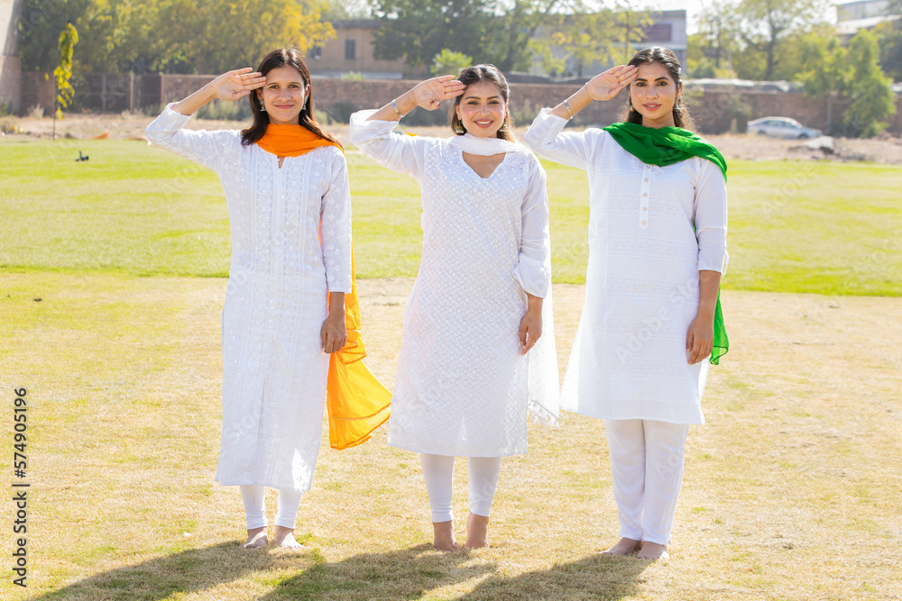 Three young beautiful girls wearing traditional white dress and saluting.standing at park celebrating indian Independence day or Republic day concept. Three young beautiful girls wearing traditional white dress and saluting.standing at park celebrating indian Independence day or Republic day concept.