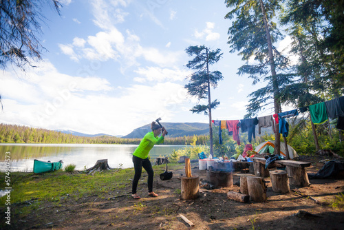 A woman chops firewood with a small axe while camping at Unna Lake in Bowron Lake Provincial Park. photo