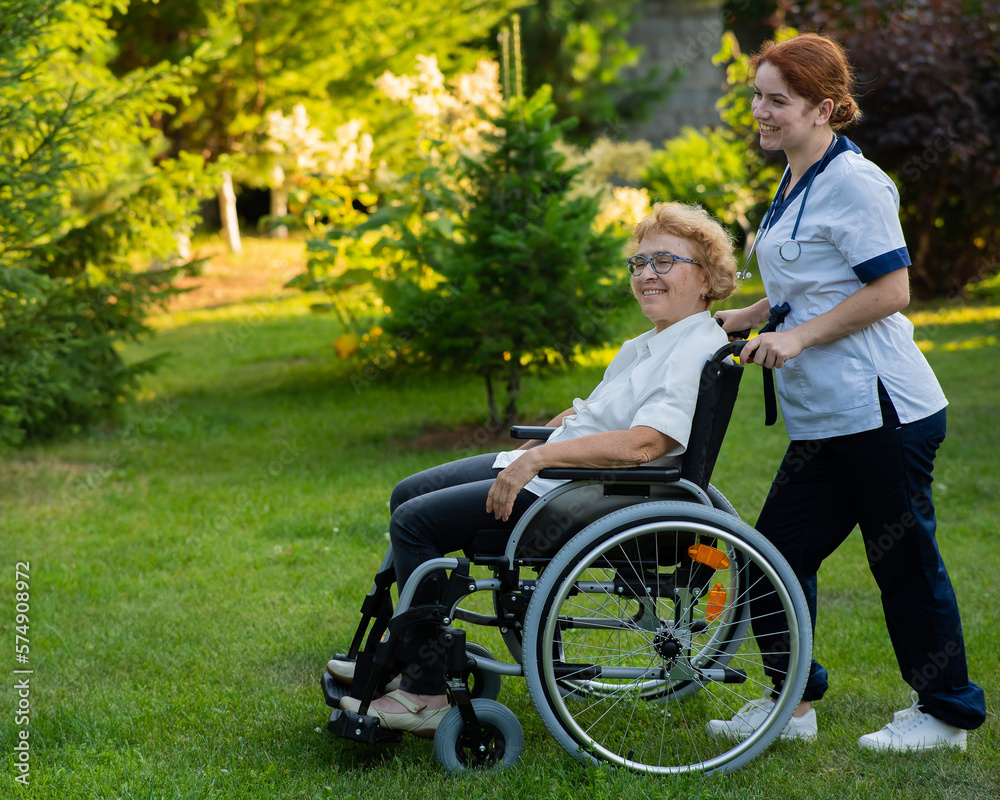 Caucasian female doctor walks with an elderly patient in a wheelchair in the park. Nurse accompanies an old woman on a walk outdoors. Caucasian female doctor walks with an elderly patient in a wheelchair in the park. Nurse accompanies an old woman on a walk outdoors.