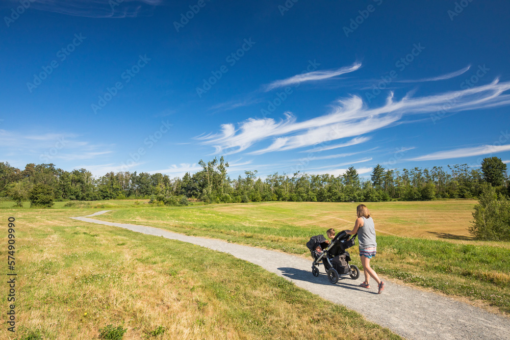 Mother pushing double stroller along dirt road in park, Langley, British Columbia, Canada Mother pushing double stroller along dirt road in park, Langley, British Columbia, Canada