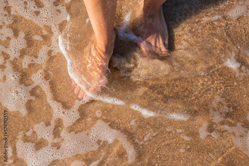 Female bare feet stand in the sea on a sandy beach. Top view, flat lay