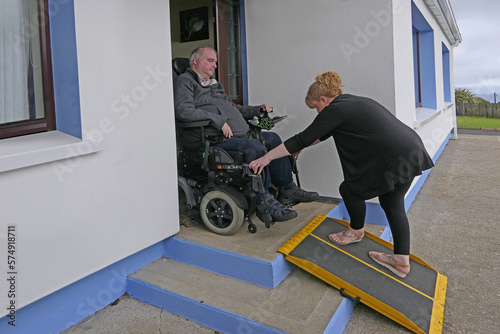 Large man in a motorised Wheelchair using a portable foldable Wheelchair Ramp on the front of building