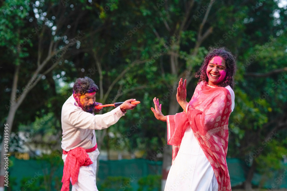 Fototapeta premium Indian man spraying color with water gun on woman at park. Holi festival concept.